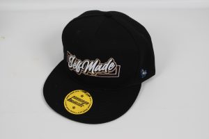 Schwarze Baseballkappe mit dem Schriftzug 'SelfMade' auf der Vorderseite und gelbem Preisetikett.