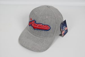 Grau Baseballcap mit rotem und blauen Schriftzug 'The American' auf der Vorderseite.