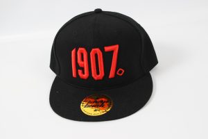 Schwarze Baseballcap mit roter Zahl 1907 auf der Vorderseite und gelbem Aufkleber.