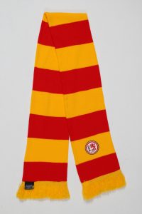 Blockstreifenschal in Rot und Gelb mit einem Wappen in der Mitte und Fransen an den Enden.