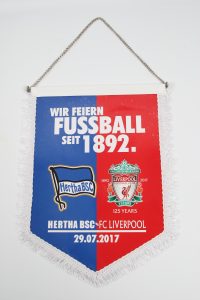 Eventwimpel mit den Logos von Hertha BSC und Liverpool FC sowie dem Text 'Wir feiern Fußball seit 1892'.