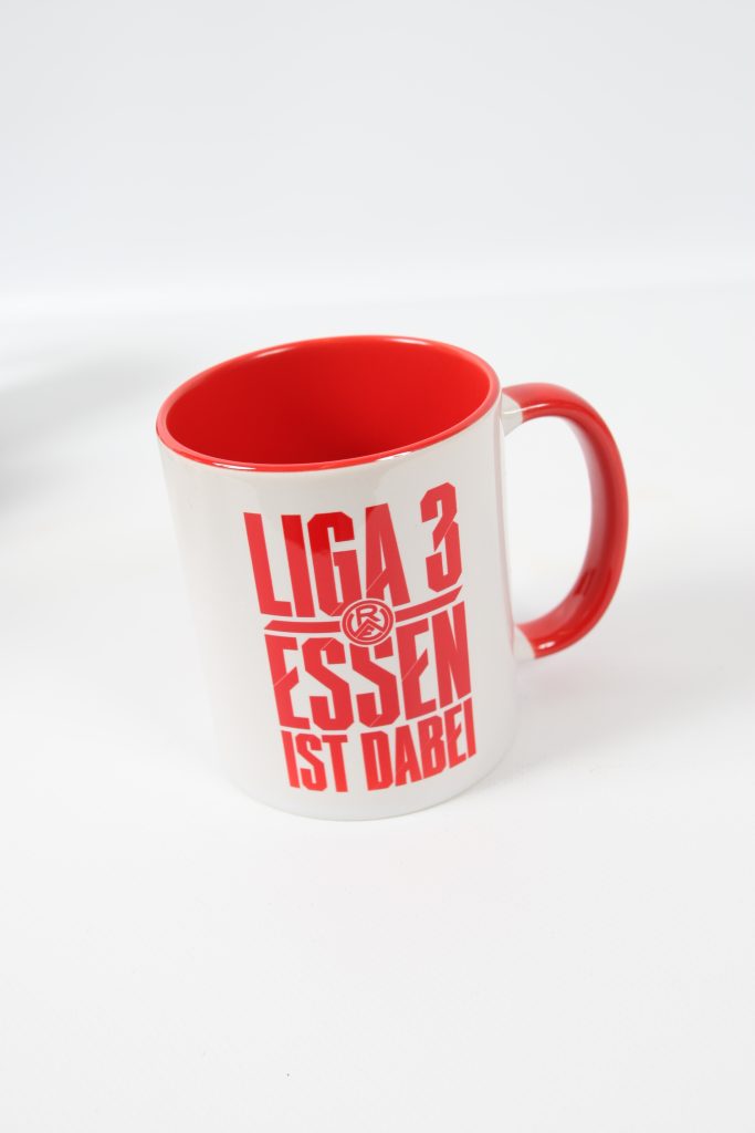 Weißer Kaffeebecher mit rotem Innenraum und dem Aufdruck 'LIGA 3 ESSEN IST DABEI'.