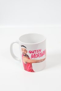 Weißer Kaffeebecher mit dem Aufdruck 'Guten Morgen' und einem abgebildeten Mann in Sportkleidung.