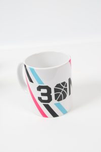 Weißer Kaffeebecher mit buntem Basketballmotiv und der Zahl 30.