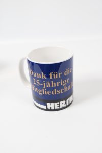 Blauer Kaffeebecher mit der Aufschrift 'Danke für die 25-jährige Mitgliedschaft' in goldener Schrift.