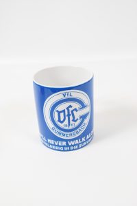 Blauer Kaffeebecher mit dem Logo des UFC Gummersbach und dem Text 'You'll never walk alone'.