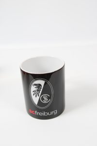 Schwarzer Kaffeebecher mit dem Logo von SC Freiburg in der Vorderansicht.