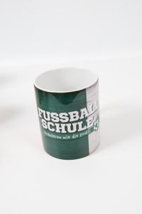 Kaffeebecher mit dem Aufdruck 'Fussballschule' in grün und weiß.