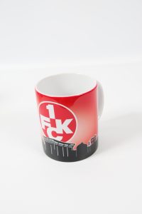 Kaffeebecher mit rotem Farbverlauf und 1FCK-Logo auf der Vorderseite.