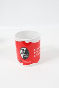 Roter Kaffeebecher mit dem Logo von SC Freiburg und dem Schriftzug 'Europapokal 22/23'.