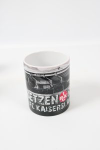 Schwarz-weißer Kaffeebecher mit dem Logo des 1. FC Kaiserslautern und Stadionansicht.