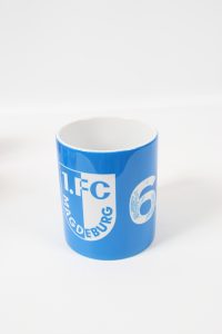Blauer Kaffeebecher mit dem Logo des 1. FC Magdeburg und der Nummer 6.