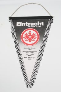 Wimpel von Eintracht Frankfurt mit dem Vereinswappen und Titeln auf schwarzem Hintergrund.
