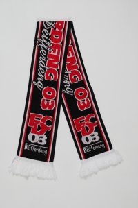 Schwarz-rot gestreifter Strickschal mit dem Logo von FC Déifferdeng 03 und Fransen an den Enden.
