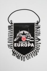 Schwarzer Wimpel mit weißen Fransen und der Aufschrift 'Zuhause in Europa'.