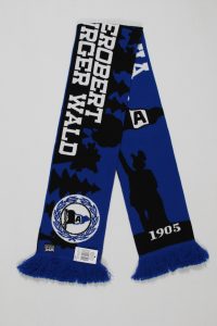 Blauer Schal mit dem Aufdruck 'Robert Gerger Wald' und einer Statue, verziert mit Fransen am Ende.