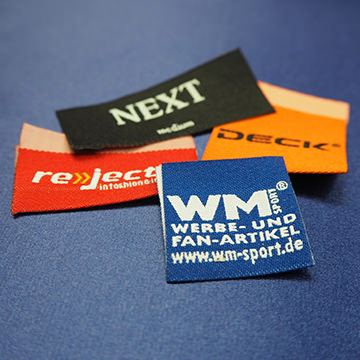 Verschiedene Textiletiketten, darunter WM-Sport, NEXT, reject und deck auf einem blauen Hintergrund.
