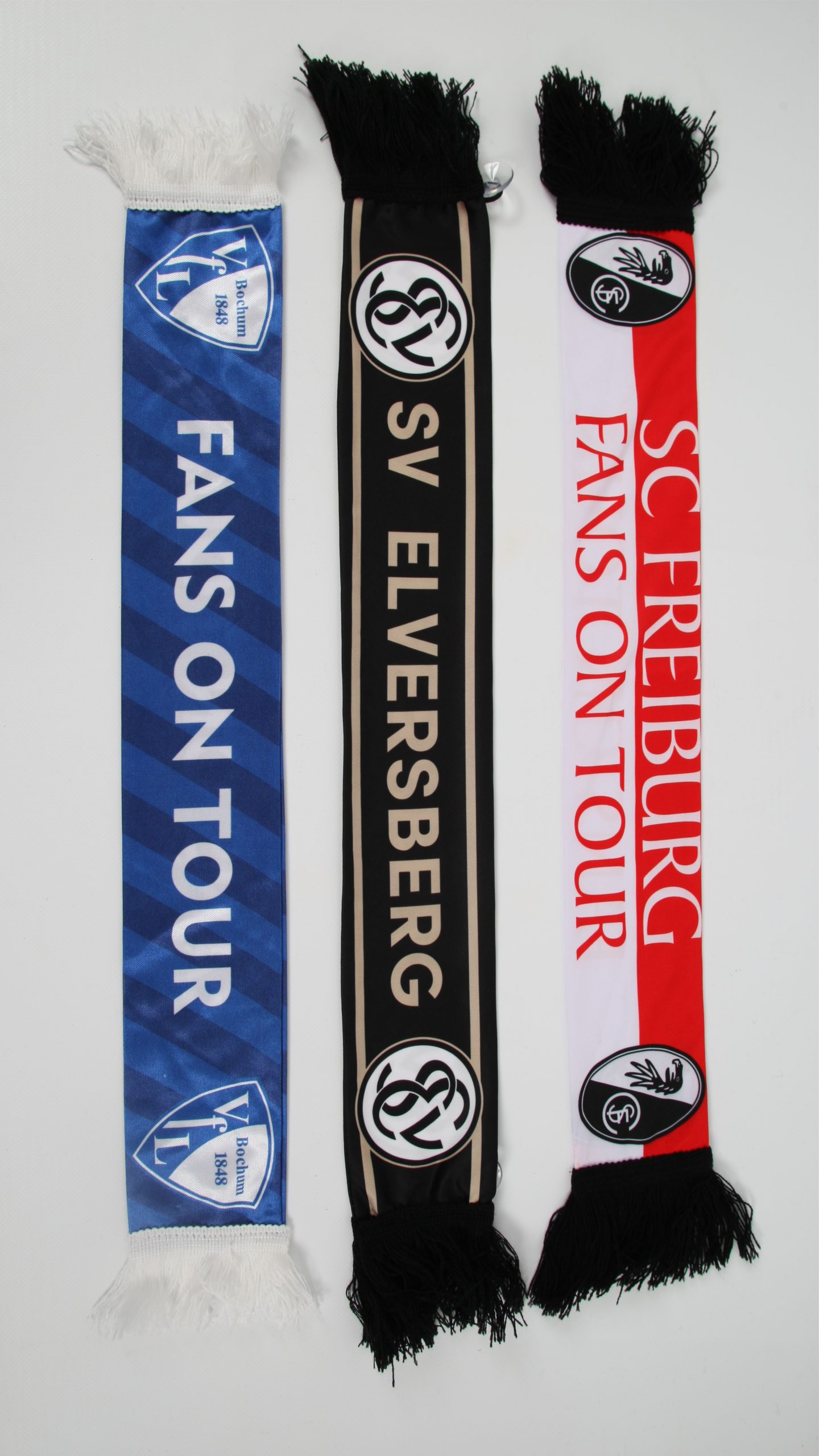 Drei Fußballschals in den Farben von SV Elversberg und SC Freiburg mit dem Schriftzug 'FANS ON TOUR'.