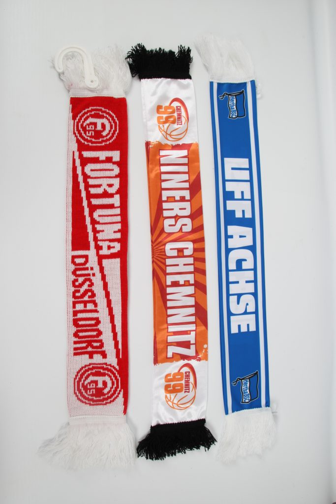 Drei Fan-Schals in den Farben Rot, Orange und Blau, jeweils mit Vereinsnamen und Wappen.