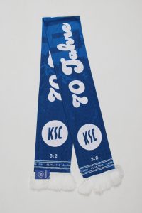 Blauer Schal mit dem Aufdruck '70 Jahre KSC' und dem Ergebnis '3:2'.