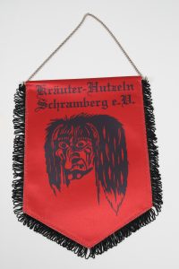 Roter Wimpel mit schwarzem Fransenrand und einem Motiv eines Gesichts auf der Vorderseite.