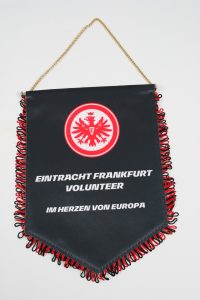 Schwarzer Wimpel mit rotem Logo von Eintracht Frankfurt und dem Text 'Volunteer' darunter.