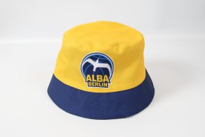 Gelber und blauer Fischerhut mit dem Logo von ALBA Berlin auf der Vorderseite.
