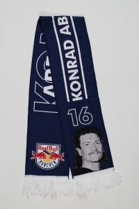 Blauer Schal mit dem Namen Konrad Abt und dem Logo von Red Bull München, verziert mit einem Porträt.