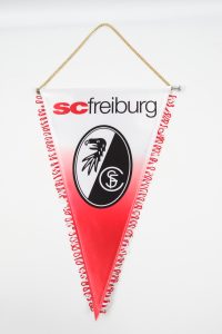 Wimpel des SC Freiburg mit dem Vereinslogo und roten Fransen.
