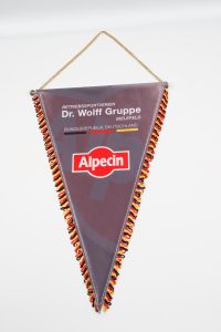 Dreieckiger Wimpel mit dem Logo der Dr. Wolff Gruppe und Alpecin in den Farben Schwarz, Rot und Gelb.