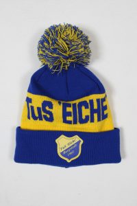Blaue und gelbe Mütze mit einem Bommel und dem Vereinslogo von TuS Eiche Harsfeld 1961.