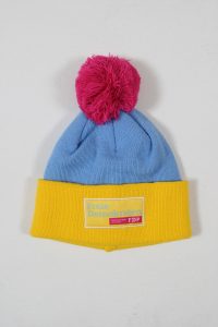 Bunte Mütze in Blau und Gelb mit einem pinken Pompon und dem FDP-Logo auf dem Umschlag.