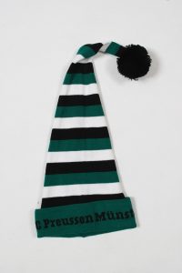 Grüne und schwarze Zipfelmütze mit weißen Streifen und einem schwarzen Bommel auf der Spitze.