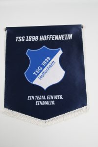 Wimpel der TSG 1899 Hoffenheim mit blauem Schild und weißem Text.