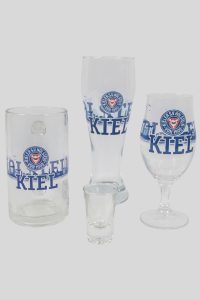 Verschiedene Gläser mit dem Kiel-Logo, darunter ein Bierkrug, ein Weizenglas, ein Schnapsglas und ein Weinglas.