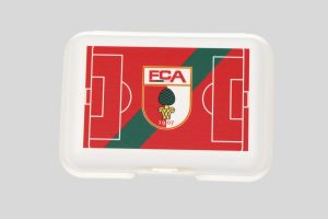 Brotdose mit dem Logo des FC Augsburg und einem Fußballfeld-Design in Rot und Grün.