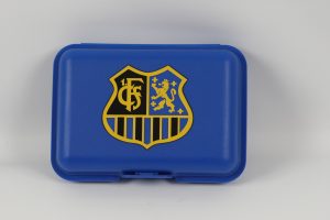 Blaue Brotdose mit einem Wappen, das einen Löwen und ein weiteres Symbol zeigt.