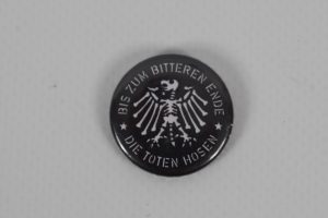 Schwarzer Button mit dem Aufdruck 'Bis zum bitteren Ende' und einem Adler-Symbol von Die Toten Hosen.