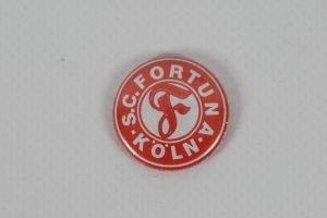Runder roter Button mit dem Logo von S.C. Fortuna Köln in weißer Schrift.