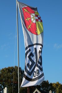 Flagge mit einem Wappen und einem Logo, die an einem Mast weht.