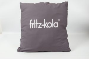 Graues Kissen mit dem Logo von fritz-kola in weißer Schrift auf der Vorderseite.