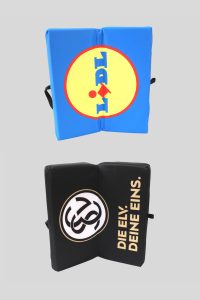 Zwei Klappkissen, eines in Blau mit LIDL-Logo und eines in Schwarz mit dem Schriftzug 'DIE ELY. DEINE EINS.'