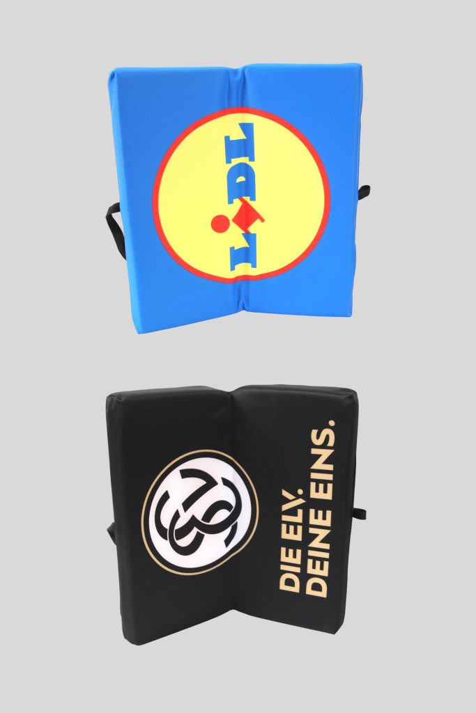 Zwei Klappkissen, eines in Blau mit LIDL-Logo und eines in Schwarz mit dem Schriftzug 'DIE ELY. DEINE EINS.'