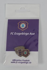 Anstecknadel des FC Erzgebirge Aue in einer Verpackung mit Vereinslogo.
