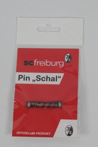 Pin mit dem Logo von SC Freiburg in einer roten Verpackung mit dem Schriftzug "OFFIZIELLES PRODUKT".