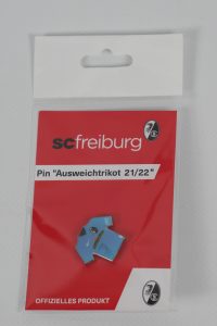 Pin in Form eines Ausweichtrikots der Saison 21/22 von SC Freiburg in einer roten Verpackung.