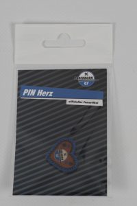 Herzförmiger Pin mit dem Logo von SC Paderborn 07 in einer transparenten Verpackung.