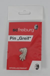 Silberner Pin in Form eines Greif mit SC Freiburg Branding auf rotem Hintergrund.