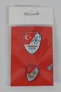 Zwei Anstecknadeln mit dem Logo von Türkgücü München auf rotem Hintergrund.