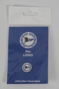 Ein Pin mit einem Logo, verpackt in einer blauen Tüte mit Aufschrift 'offizieller Fanartikel'.